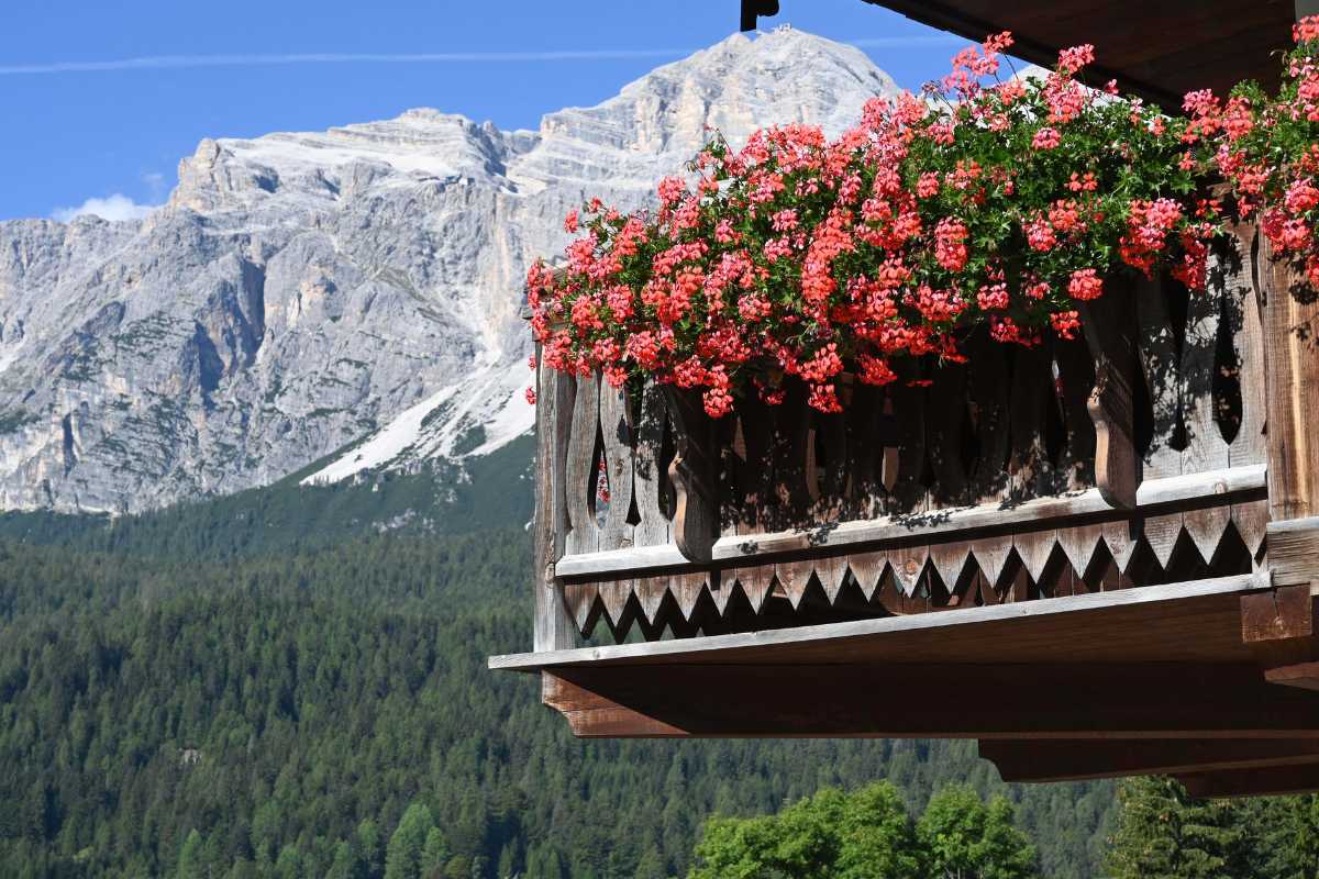 Panoramica del centro di Cortina d'Ampezzo con le Dolomiti sullo sfondo, atmosfera vivace, dettagli di palazzi storici e chiesa parrocchiale.